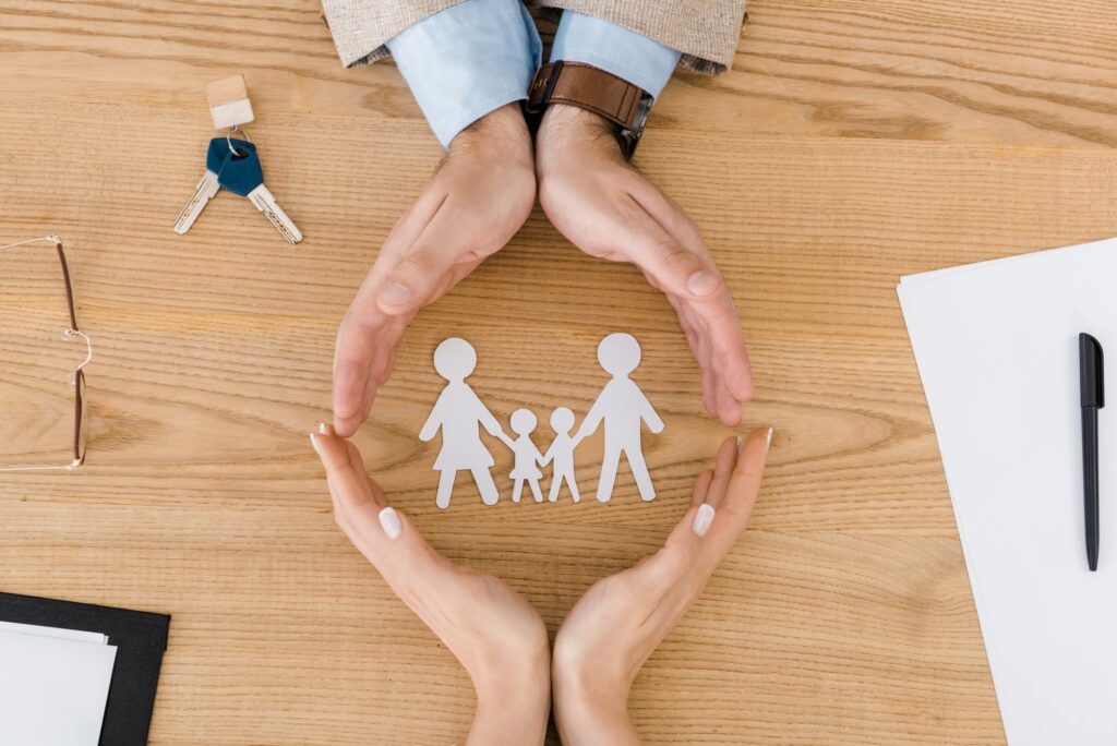 Couple making circle with hands on wooden table with paper people inside, family insurance